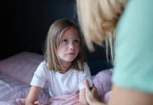 Mother talking to sad little girl in bed. Psychological support for children concept